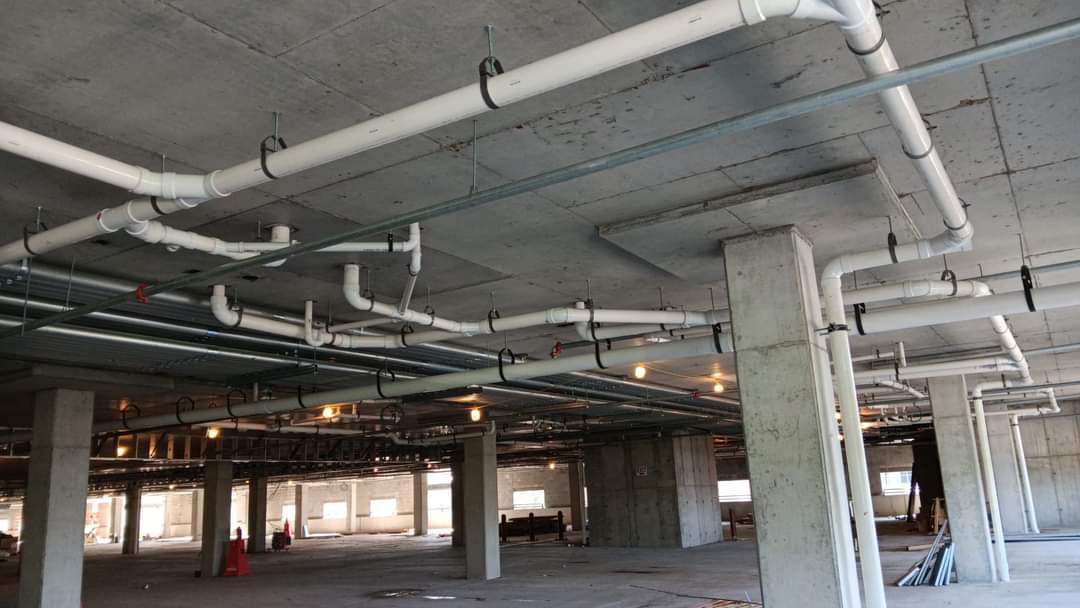 New drain and vent piping hung from the ceiling of a commercial parking garage