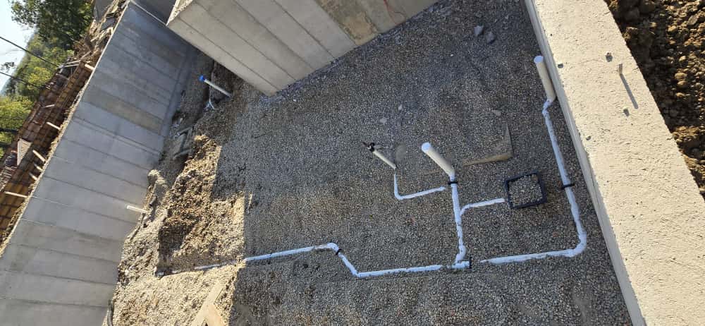 New white drain lines laid in gravel inside a basement before the slab is poured