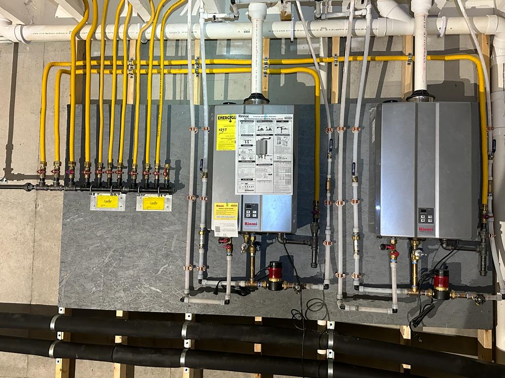 Two tankless water heaters mounted and piped on a basement wall